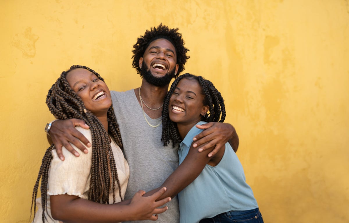 Three family members hug each other in front of a yellow wall